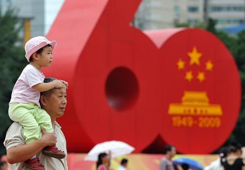 10月1日,一位市民带着孩子经过福州街头的新中国成立60周年国庆庆祝活动标志。十一长假期间,各地国庆游园活动中、广场绿地上随处可见孩子们的可爱身影。对纯真的儿童而言,十一是祖国母亲的生日,也是他们的快乐假期。新华社记者 姜克红摄